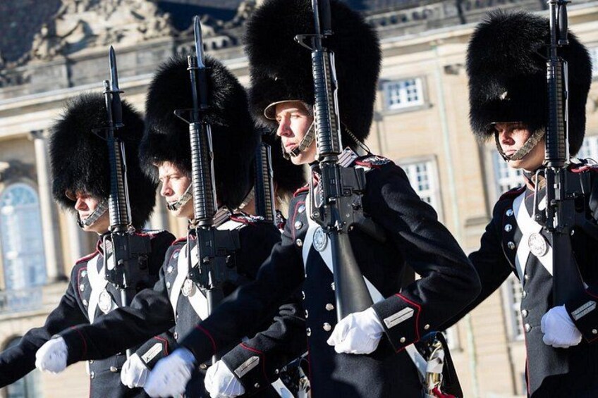 Guards in uniform with rifles, wearing tall black hats with fur trim, standing in front of a building with classical architecture. 2