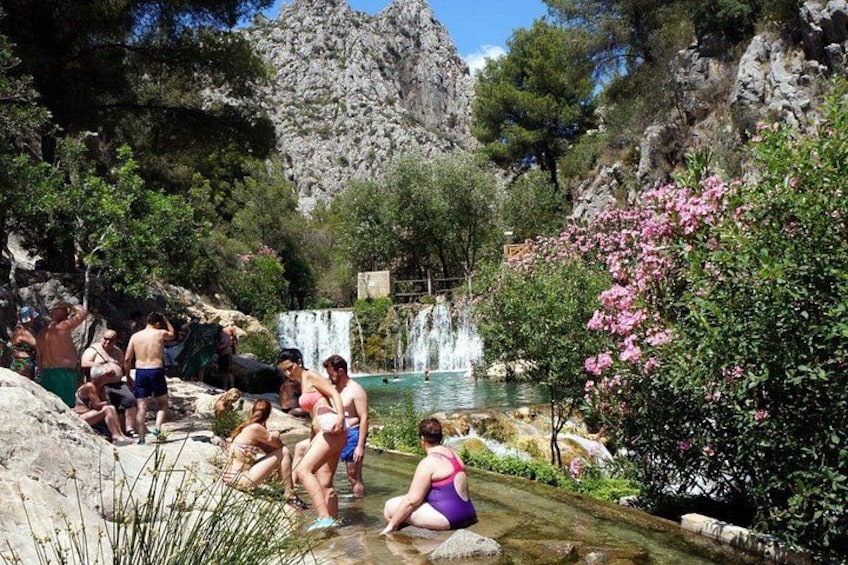 A natural pool with people swimming and relaxing, surrounded by rocky terrain and trees. 5