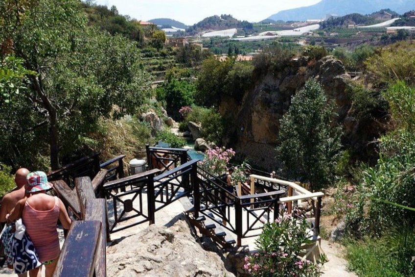 A rocky terrain with wooden structures, a person in a red dress, and a scenic valley with mountains in the background. 2
