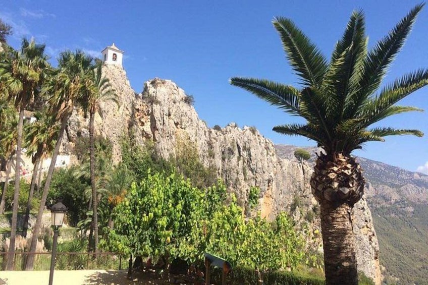 A rocky cliff with a bell tower, palm trees, and a clear blue sky. 2
