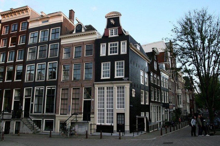 Una hilera de edificios históricos con estilos arquitectónicos diversos, incluyendo un frente blanco y negro y un techo de tejas rojas. 5