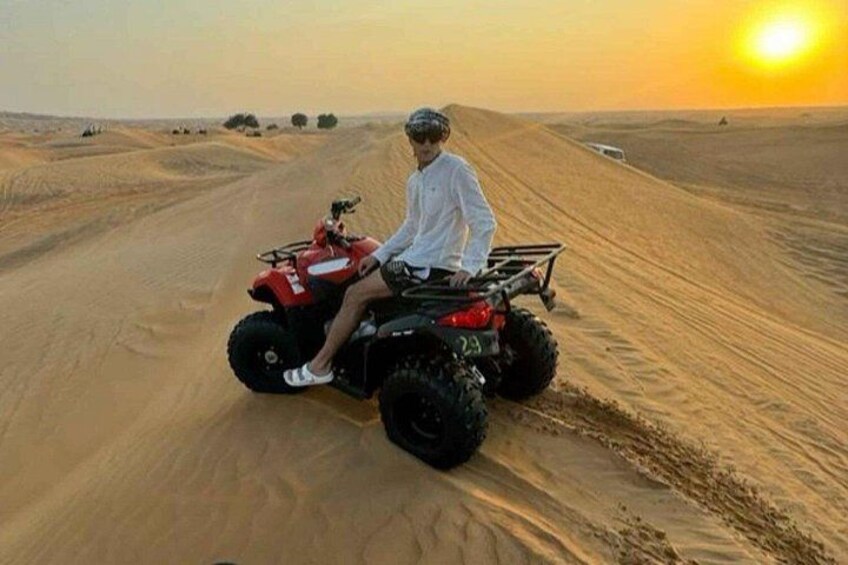Una persona guida un quad rosso su una duna sabbiosa al tramonto. 4