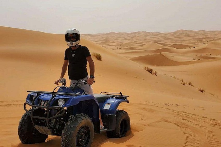 Una persona su un quad blu in un deserto con dune di sabbia. 1