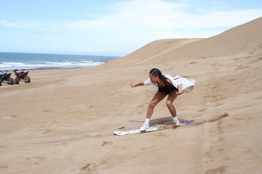 Una persona fa snowboard su una discesa sabbiosa, con una spiaggia e l'oceano sullo sfondo. 5