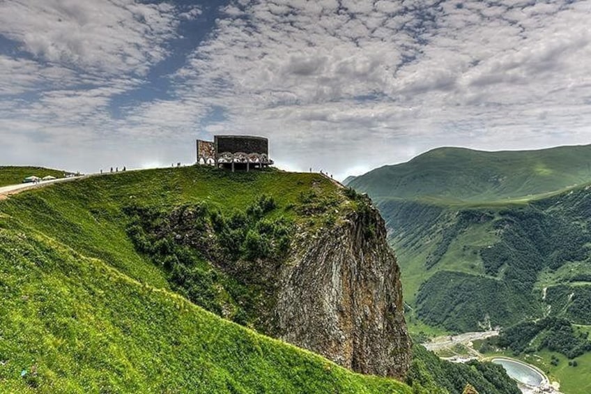 Un bâtiment perché au bord d’une falaise, une route sinueuse et une vallée verdoyante. 3