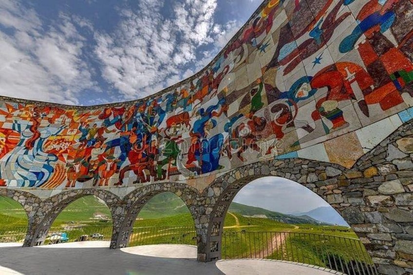 Une fresque colorée orne une structure en pierre aux formes arrondies et dotée d’arches, le tout se détachant sur un ciel dégagé. 2