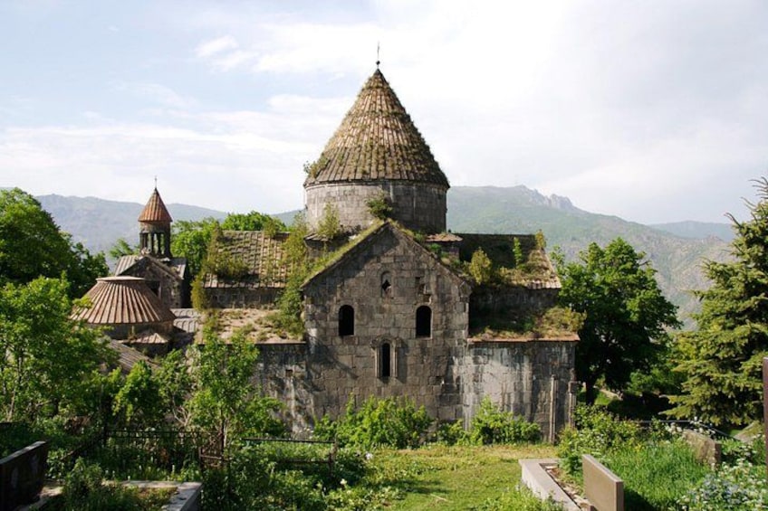An ancient stone church with a conical roof, surrounded by lush greenery and mountains in the background. 5