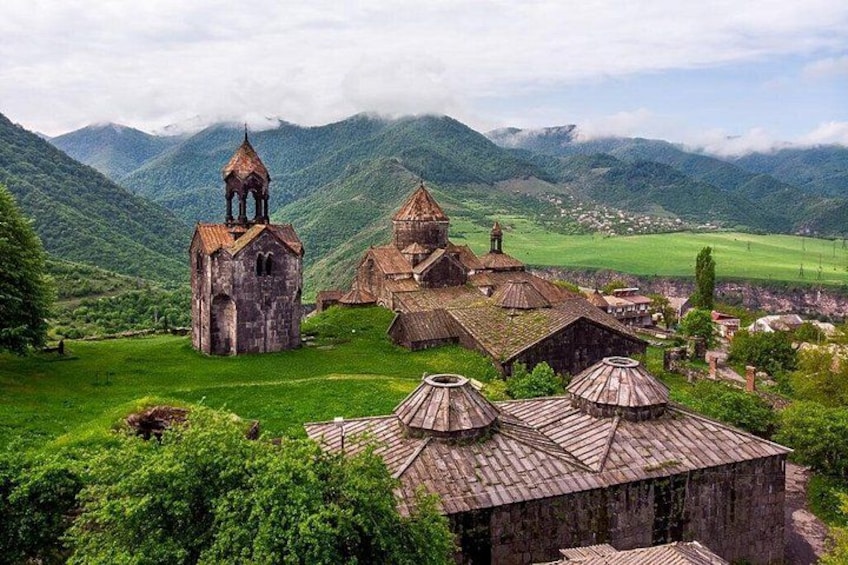 A rural village with traditional architecture, including a church with a bell tower, surrounded by lush green hills. 1