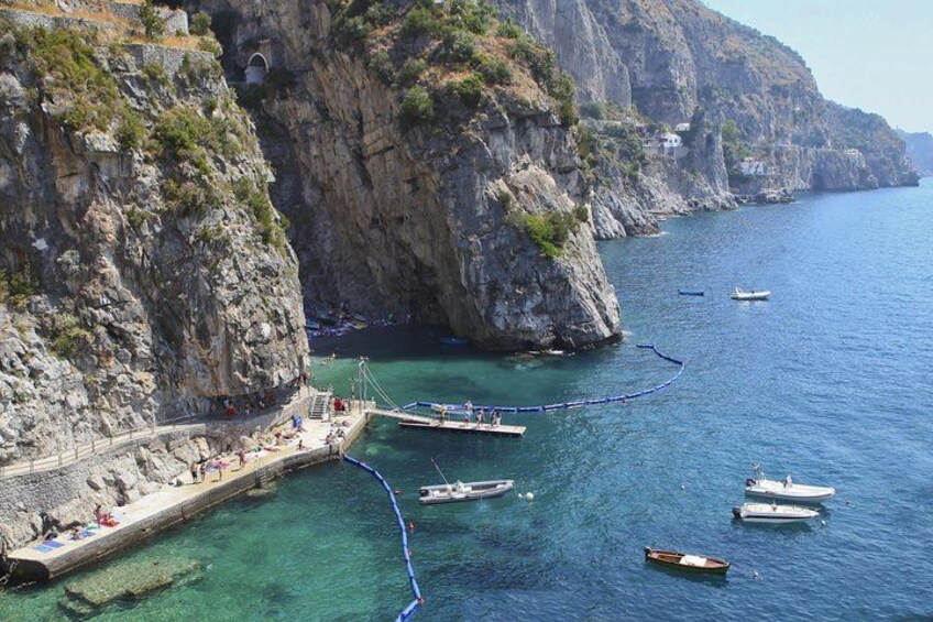 A coastal area with rocky cliffs, a pier, and several boats in the water. 1
