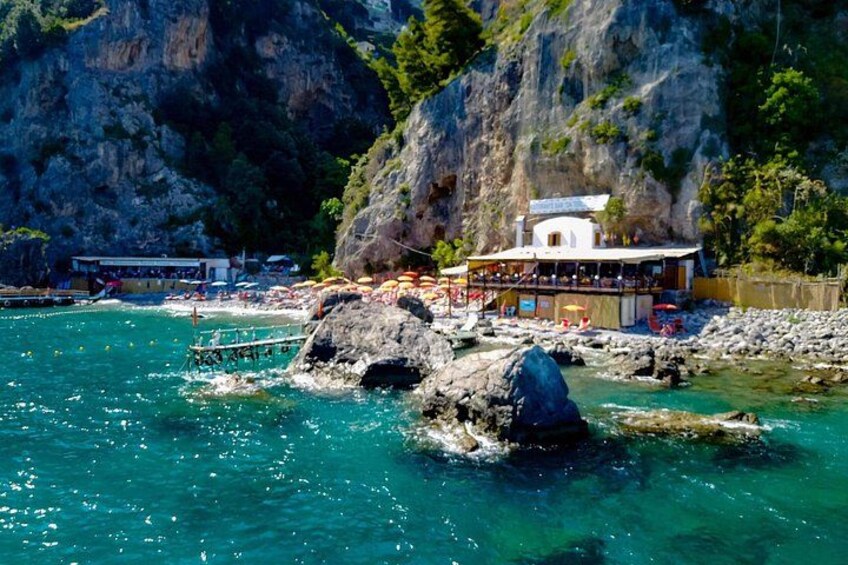 A coastal area with rocky terrain, clear turquoise water, and a building with a balcony overlooking the sea. 4
