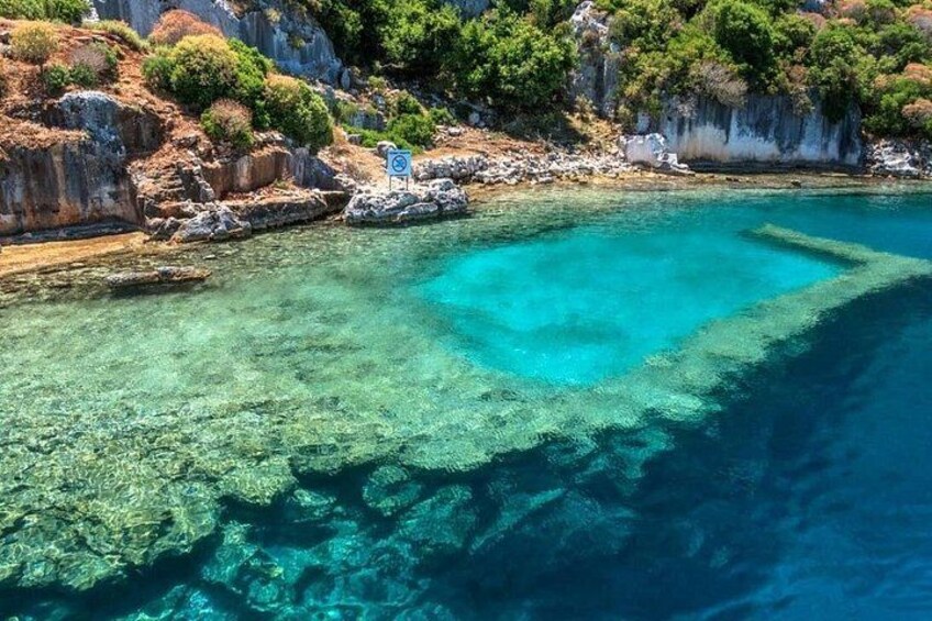 A coastal area with clear turquoise waters, rocky cliffs, and sparse vegetation. 3