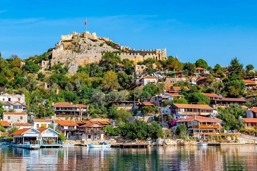 A coastal town with a prominent castle on a hill, waterfront buildings, and boats docked at the pier. 1
