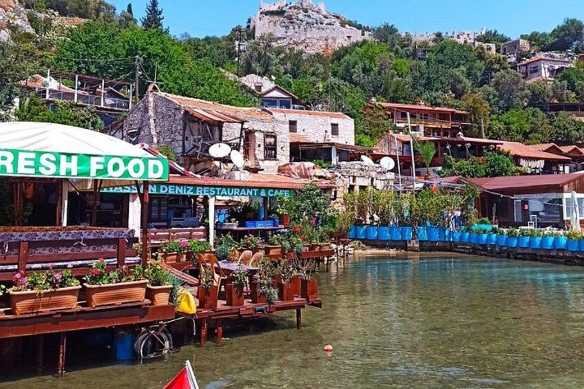 A waterfront restaurant with outdoor seating, a sign reading 'FRESH FOOD,' and a mountainous backdrop. 5