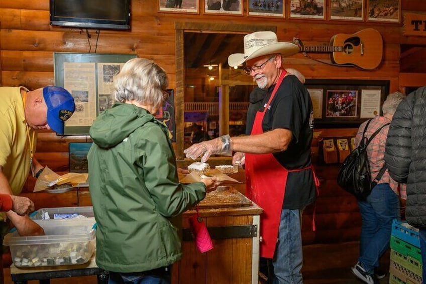 A man in a cowboy hat and apron serving food at a counter in a rustic wooden building with a guitar in the background. 2