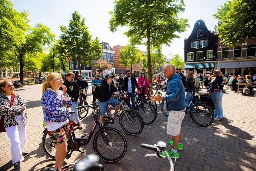 Un grupo de personas en bicicleta en una plaza pública con árboles y edificios al fondo. 4
