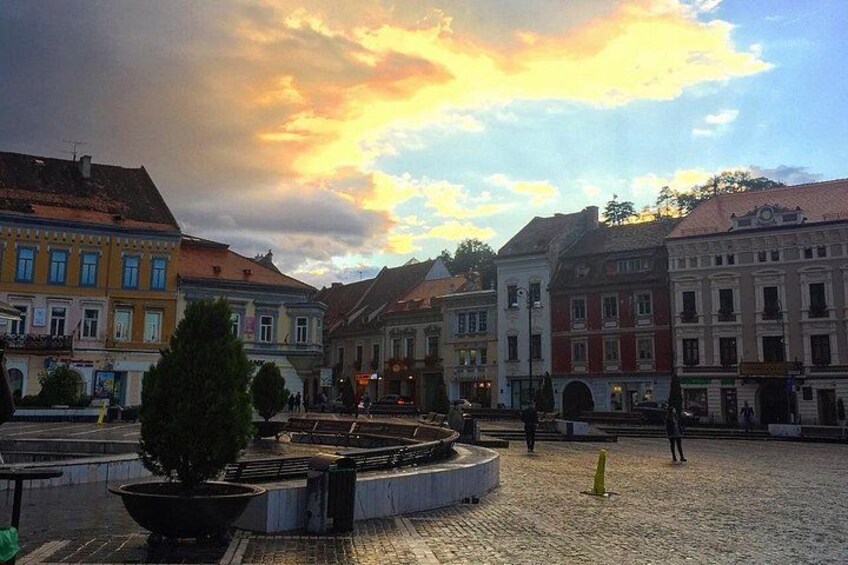 Une place pavée, bordée de bâtiments historiques, avec une fontaine et un ciel au coucher du soleil. 5
