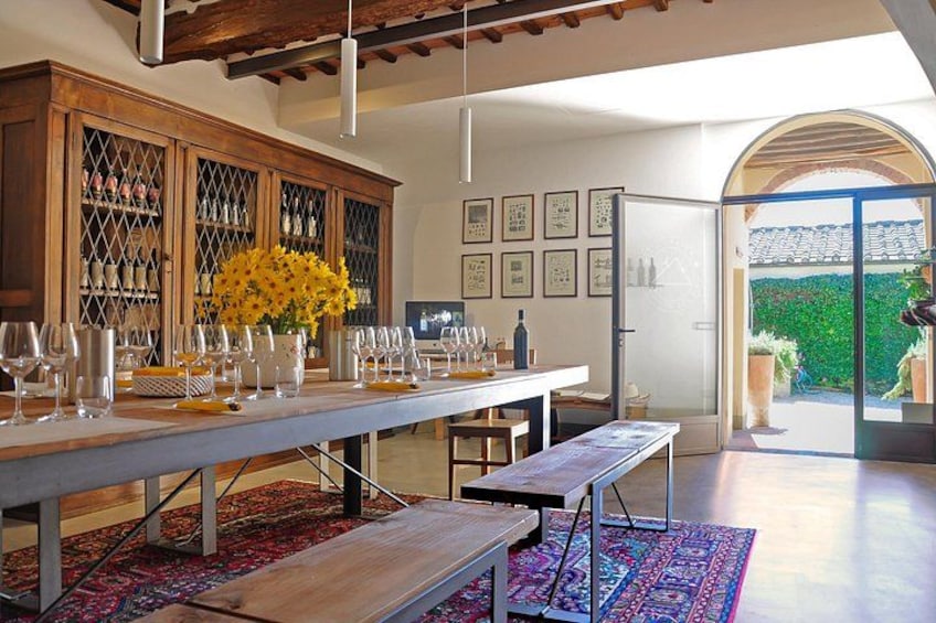 Un comedor con una larga mesa dispuesta para una comida, un mueble de madera con puertas de vidrio y vistas a un jardín a través de un ventanal. 2