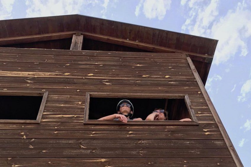 A wooden building with two windows and a person leaning out of one window. 2