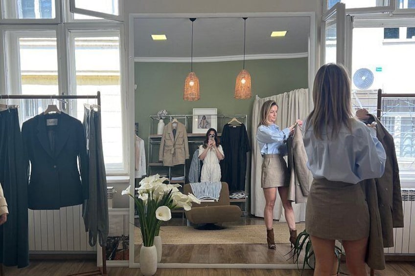 A clothing store interior with racks of clothes, a mirror, and a vase with flowers. 2
