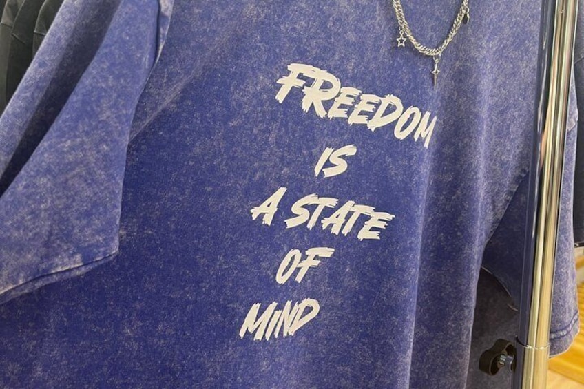 Una camisa azul con el texto 'FREEDOM IS A STATE OF MIND' y un pequeño logo 'M'. 2