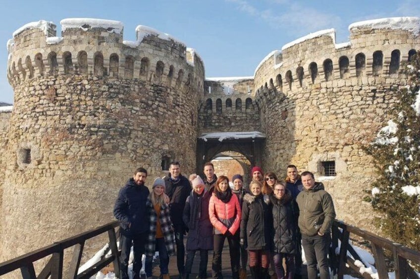 Eine Gruppe von Menschen steht vor einer Steinschlossburg mit zwei runden Türmen und einer Holzbrücke. 4
