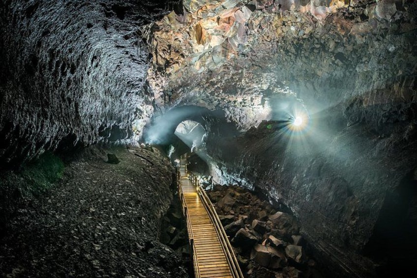 A cave with a wooden walkway and a light source at the end. 4