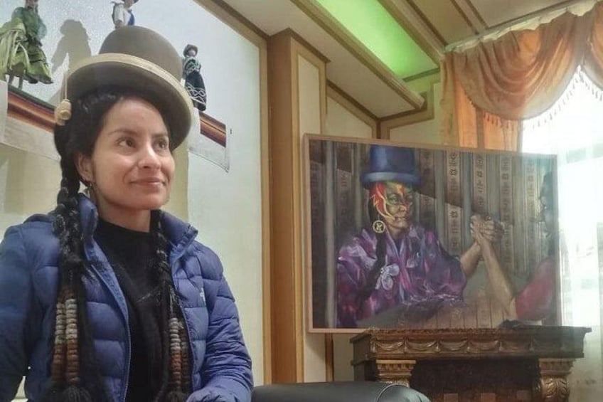 A person in a blue jacket and hat sitting in front of a painting. 3