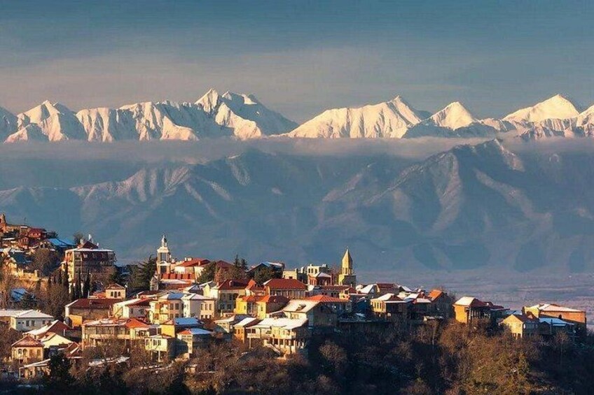 A mountainous town with snow-capped peaks in the background and a church with a bell tower in the foreground. 4