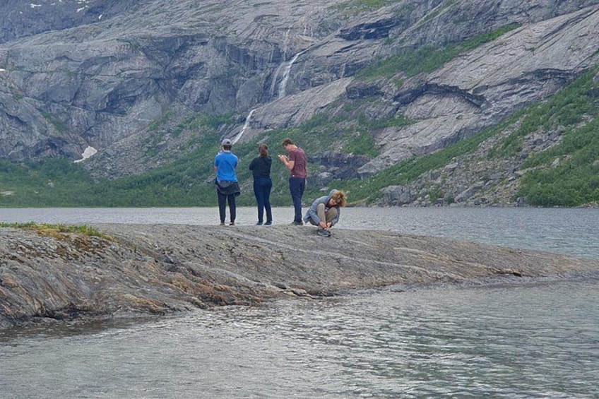 Een groep mensen staat langs een rotsachtige kustlijn, met een waterval op de achtergrond. 3