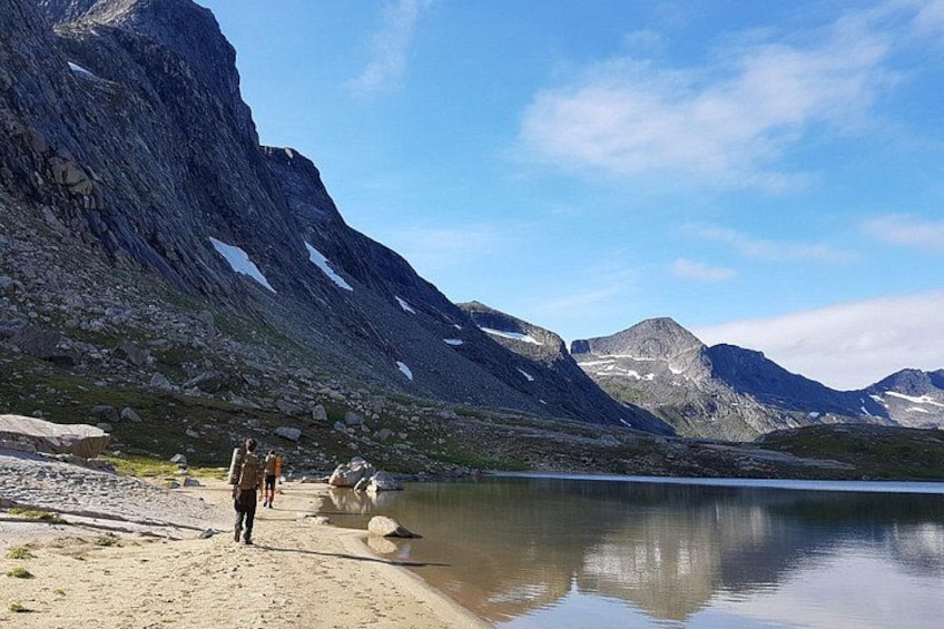 Een bergachtig landschap met een meer, rotsachtig terrein en enkele mensen die langs de oever lopen. 4
