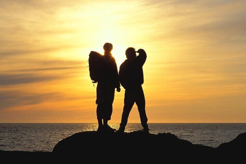 Two people silhouetted against a sunset, standing on a cliff by the sea. 4
