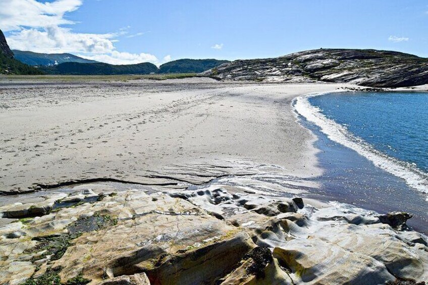 A coastal landscape with a sandy beach, rocky outcrops, and a clear blue sea. 3