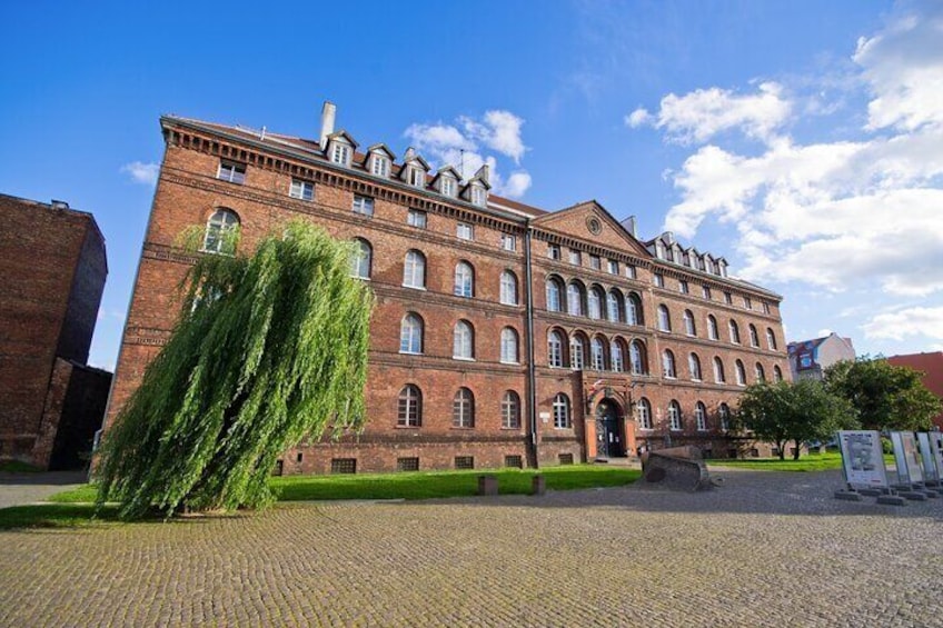 A large brick building with multiple windows and a green tree in front. 3
