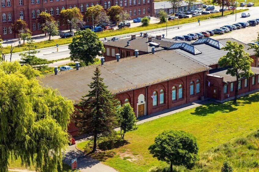 A red brick building with a flat roof and arched windows, surrounded by trees and a parking lot. 4