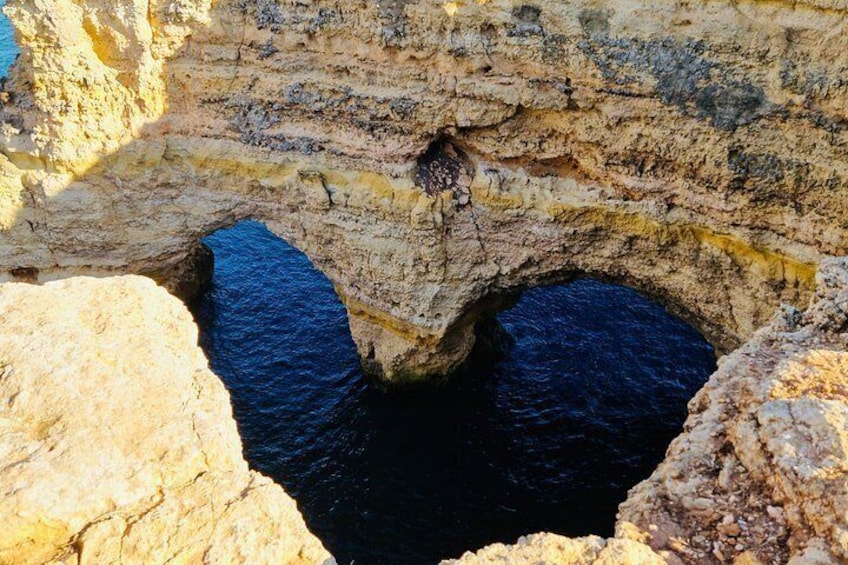 A coastal rock formation with two natural arches and a narrow passageway. 3