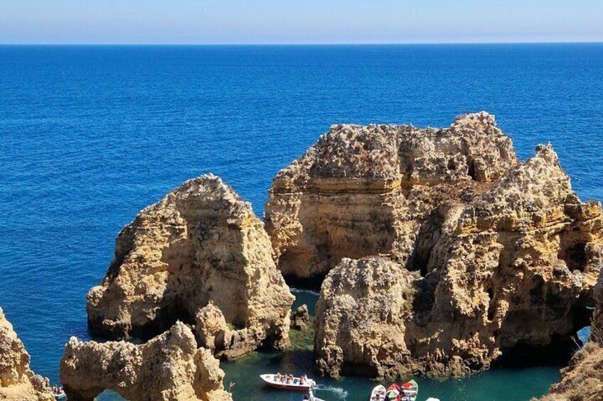 A rocky coastal landscape with clear blue sea, a boat in the foreground, and a clear sky. 4