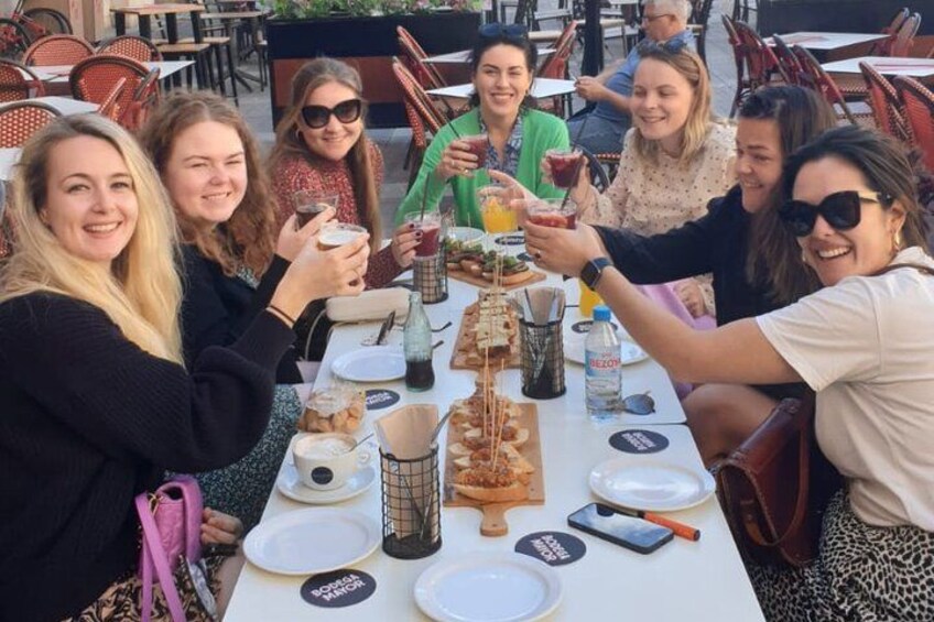 Un groupe de personnes est assis autour d’une table, à l’extérieur, et partage un repas et des boissons. 3
