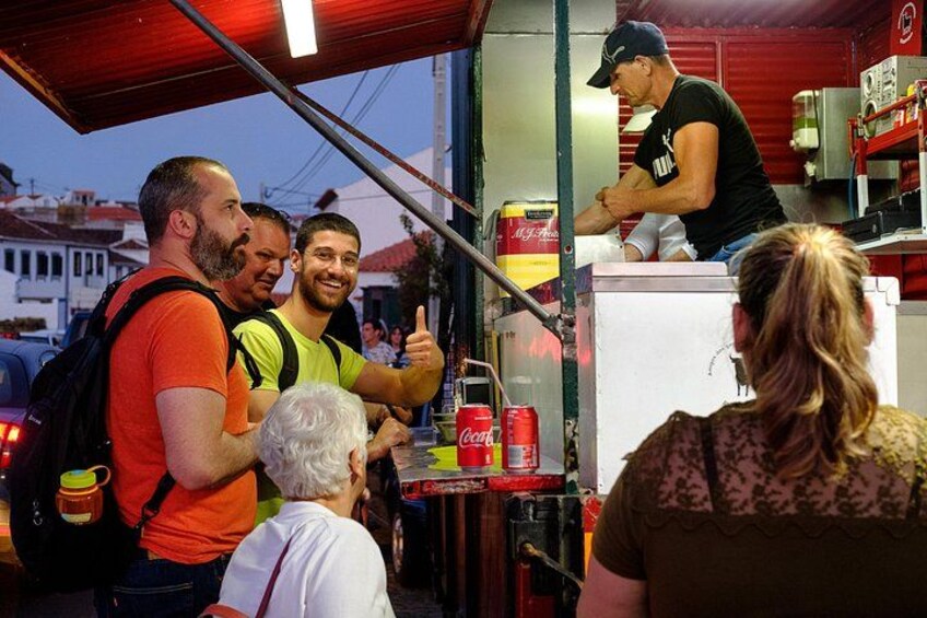 A group of people at a food stall with a man serving food. 1