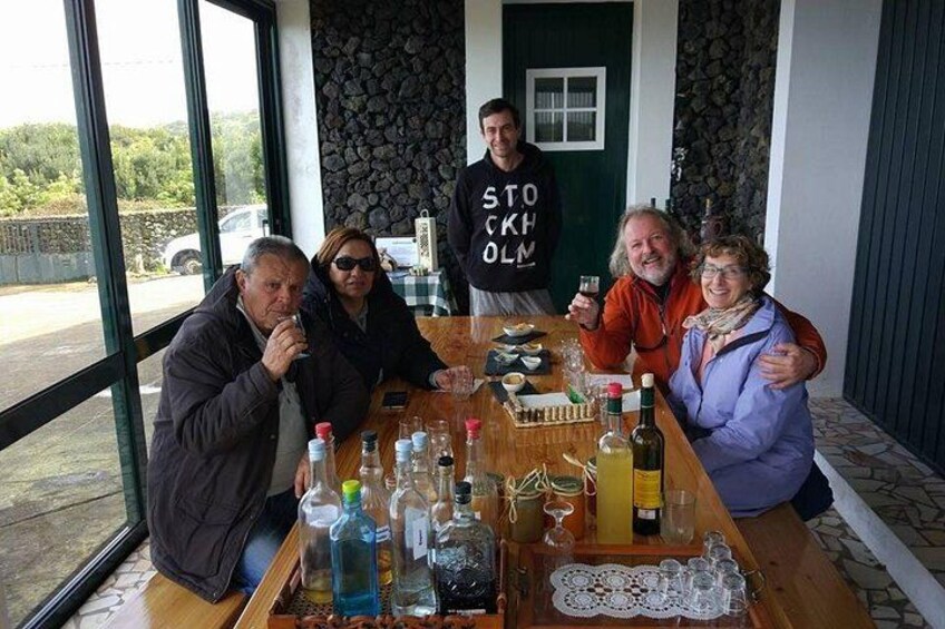 A group of people sitting at a table with bottles and glasses, in a room with a stone wall and a window. 2