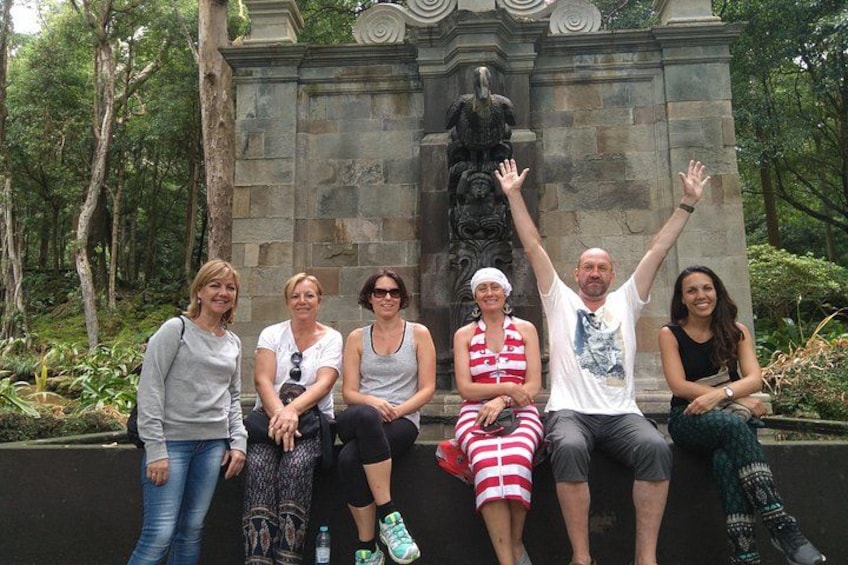 A group of people sitting on a bench in a park with a stone monument in the background. 5