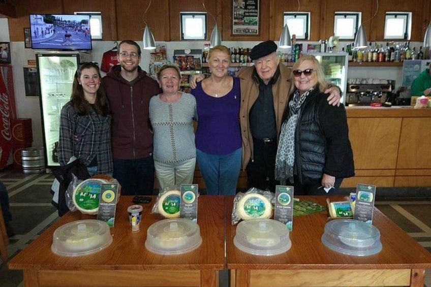 A group of people standing in a store with cheese displays on a wooden table. 4
