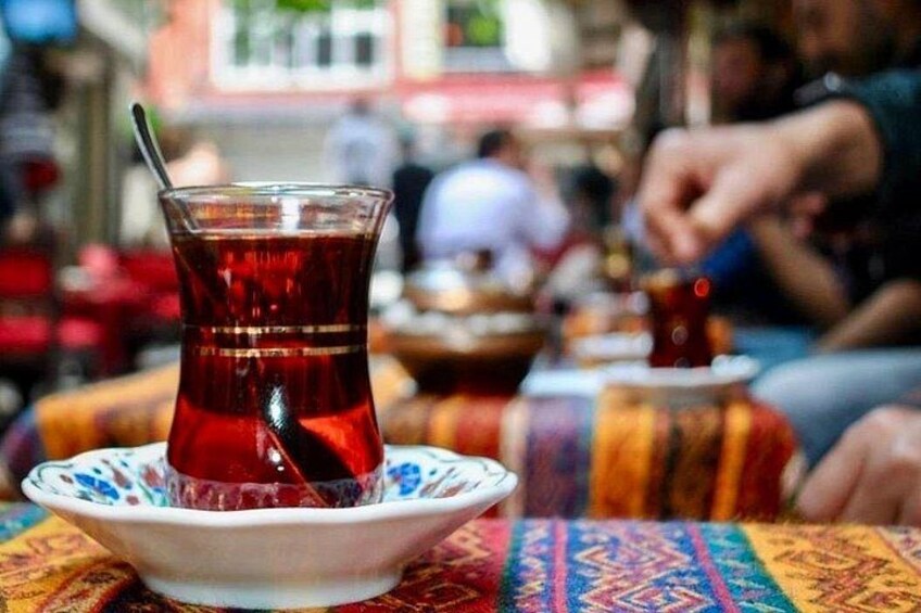 A glass of tea on a patterned tablecloth with a spoon, set in a busy outdoor dining area. 4