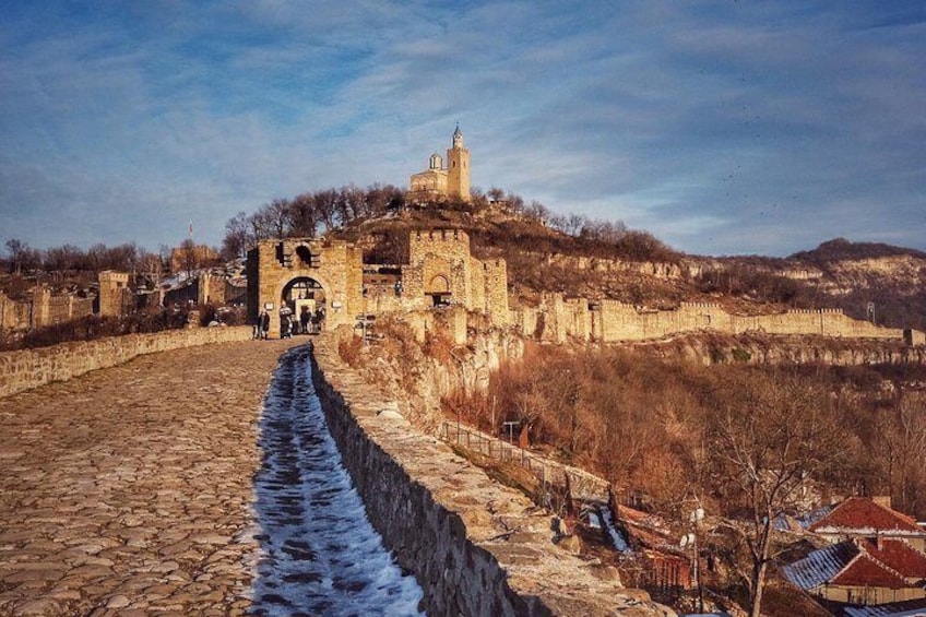 A historic stone bridge leading to a fortified castle with a tower, surrounded by barren hills. 1