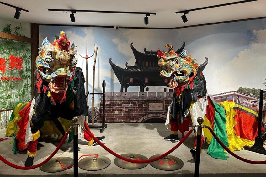A traditional Chinese lion dance performance with performers in elaborate costumes and masks, set against a backdrop of a painted Chinese architectural scene. 4