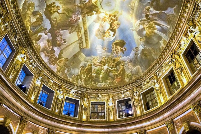 An ornate interior with a domed ceiling, gold detailing, and classical frescoes. 4