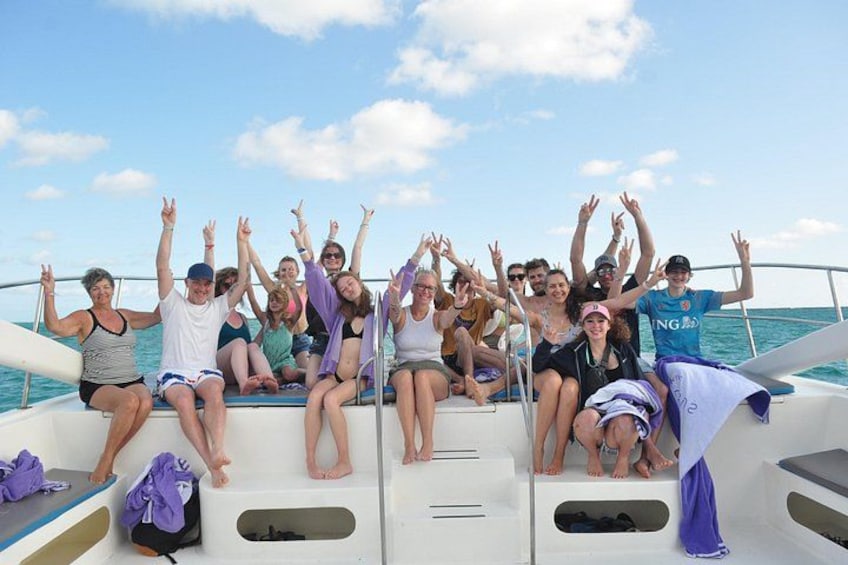 A group of people on a boat with raised hands, wearing casual summer clothing, and the ocean in the background. 5