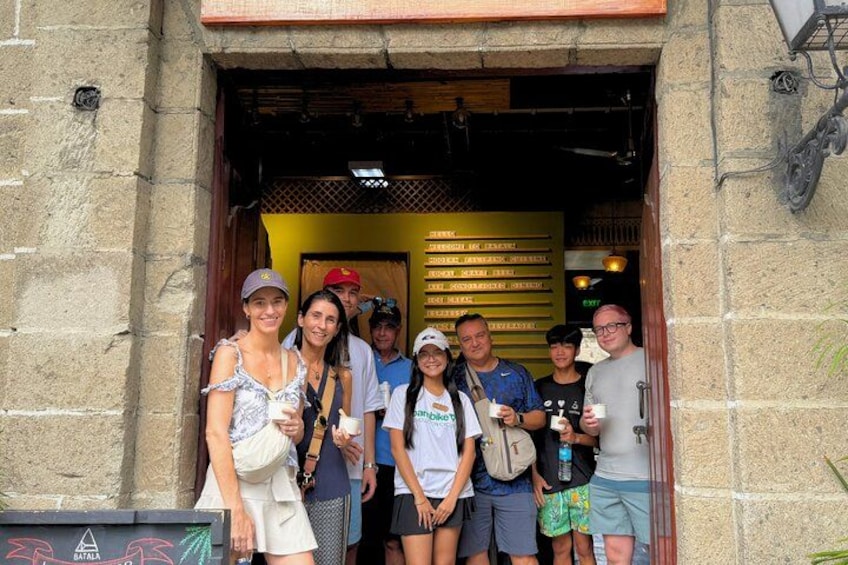 A group of people standing at the entrance of a building with a yellow sign and a metal gate. 2