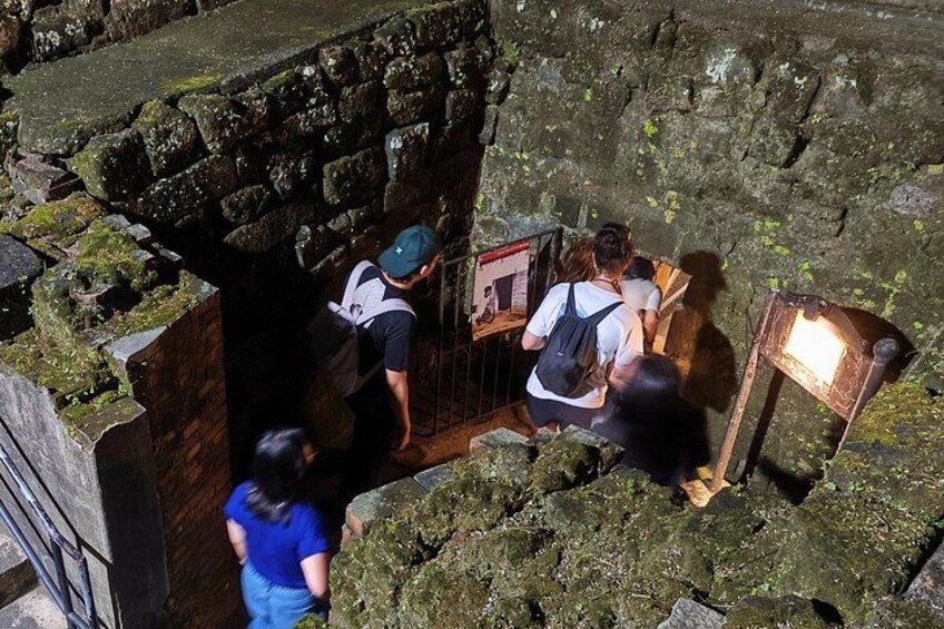 Un grupo de personas en un sitio histórico con muros de piedra y un letrero de madera. 3