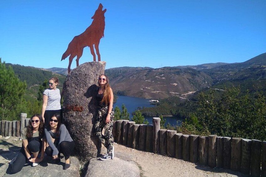 Un groupe de personnes posant à côté d’une statue de loup, sur un promontoire rocheux surplombant une vallée. 2