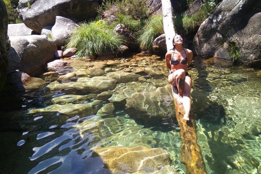 Une personne assise sur un rocher, au bord d’un ruisseau aux eaux claires, entourée de rochers et de verdure. 3